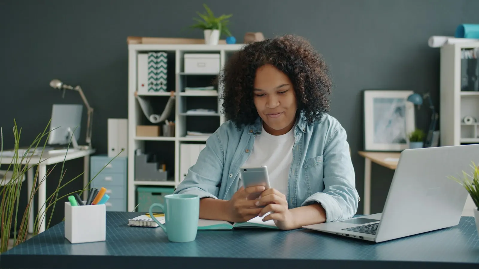 A young woman types a message on her phone at a desk
