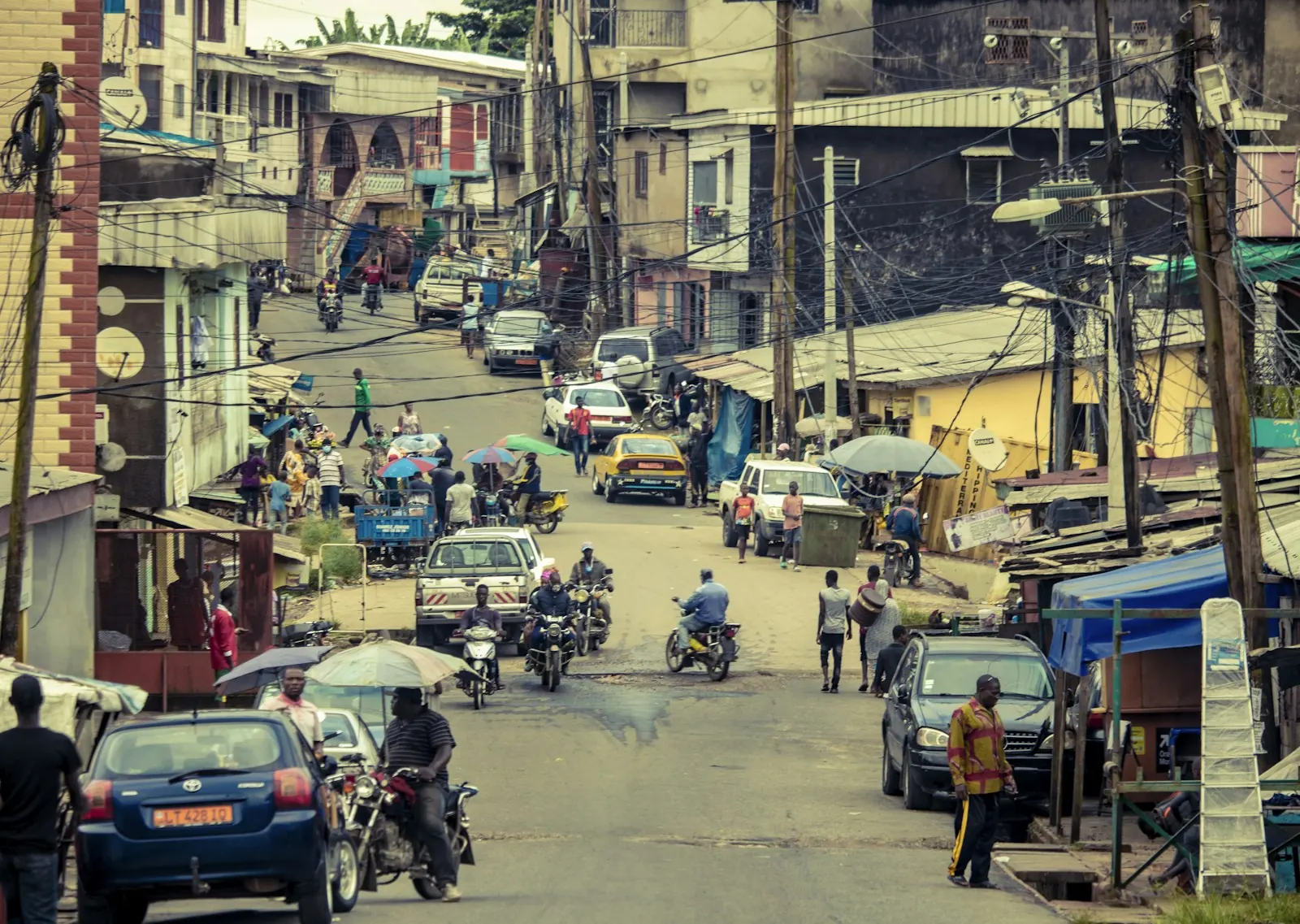 A busy hillside street in Cameroon with cars, motorbikes and people walking