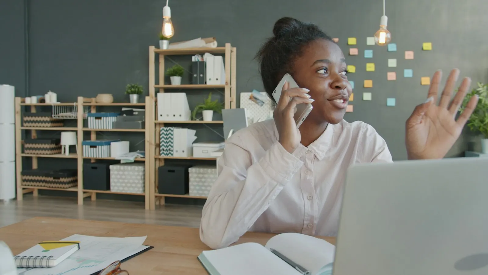 A professional woman on a phone call at her desk, with a laptop and notebook